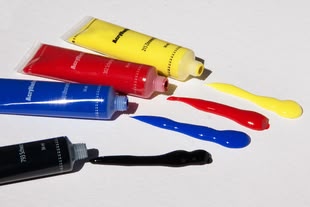 vier Acrylfarben liegen geöffnet auf einer weißen Oberfläche.
