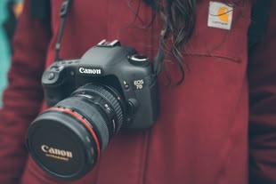 Kamera zurücksetzen nicht vergessen! Foto: Mario Calvo/Unsplash. Eine Kamera hängt um den Hals einer Person.