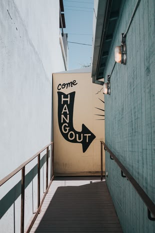 Fotografieren lernen im Fotokurs: Reisefotografie. Foto: Tyler Nix/Unsplash. Die Fotografie zeigt eine Gasse, an dessen Ende sich ein Schild befindet, auf dem geschrieben steht: ,,come hangout”.