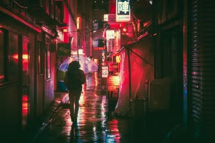 Fotografieren bei Regen ergibt spannende Motive. Fotografieren lernen im Fotokurs. Foto: Masashi Wakui/Pixabay License. Eine Person mit Regenschirm läuft durch eine beleuchtete Straße.