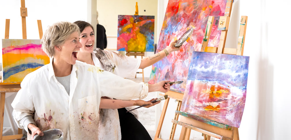 Dozentin Tanja Strickrot und Teilnehmerin stehend lachend vor einem Gemälde