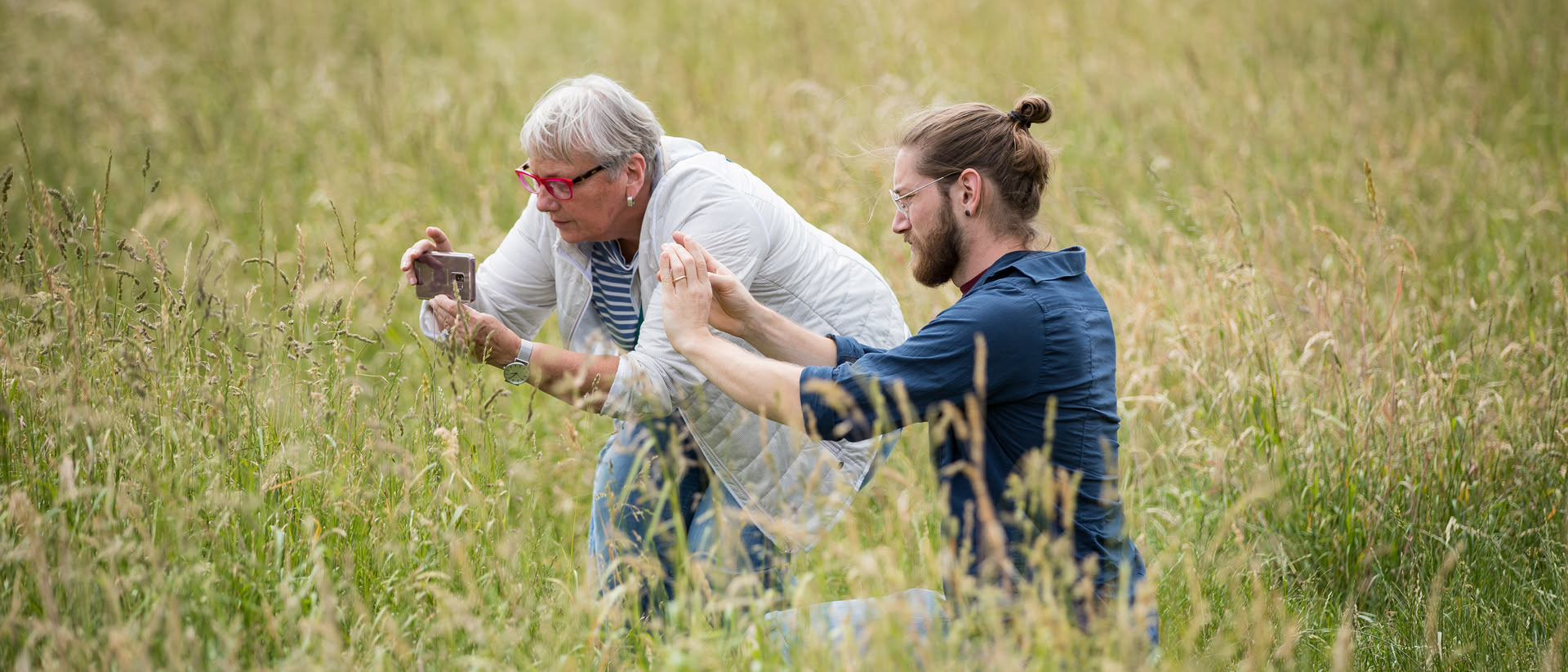 Dozent Sebastian Hopp und eine Kursteilnehmerin stehen in einem Feld und fotografieren mit ihren Smartphones