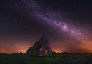 Auf dem Foto ist ein Sternenhimmel über einem Gebäude auf einer Wiese abgebildet.