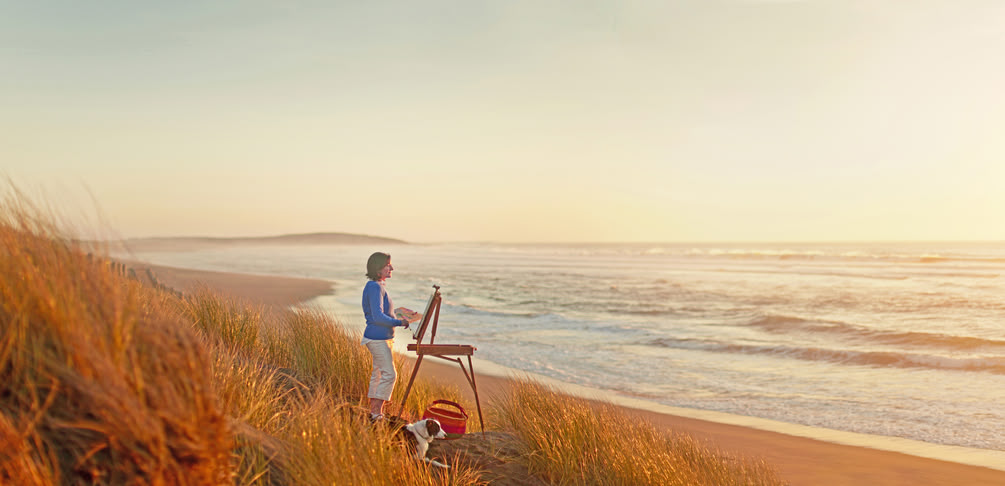 Frau malt an der Staffelei mit Blick auf das Meer
