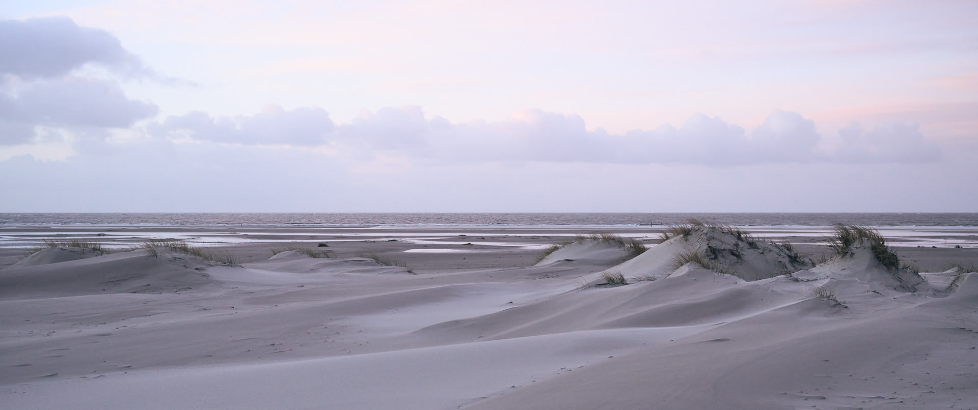 Eine Dünenlandschaft am Abend bei bewölktem Himmel.