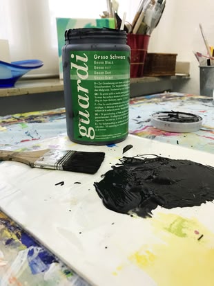 Ein Gefäß mit guardi Gesso Schwarz steht auf einem Tisch, davor ein Pinsel, der darin getaucht wurde