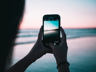 Mit einem Handy wird das Meer während eines Sonnenunterganges fotografiert.