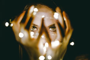 Das Licht ist der wichtigste Faktor in die Fotografie. Fotografieren lernen im Fotokurs. Foto: Rhett Wesley/Unsplash. Fotografie einer Frau, die ein leuchtendes Objekt in den Händen hält. Das Bild ist hauptsächlich in Orange- und Grüntönen gehalten.