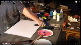 Tipps und Tricks Pastellpapier selber machen, Bild: Schmincke Screenshot aus dem Youtube-Video von Schmincke “SCHMINCKE Profi-Tipp: Pastellgrundierung”: eine Arbeitsfläche, auf der eine Vielzahl an Materialien, die man zum Malen benötigt, liegen.