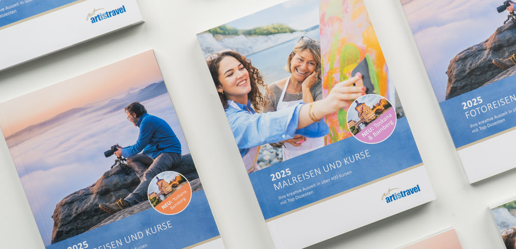 artistravel-Kataloge liegen auf dem Tisch und sind abwechselnd zu sehen - Malreisen Katalog und Fotoreisen Katalog.