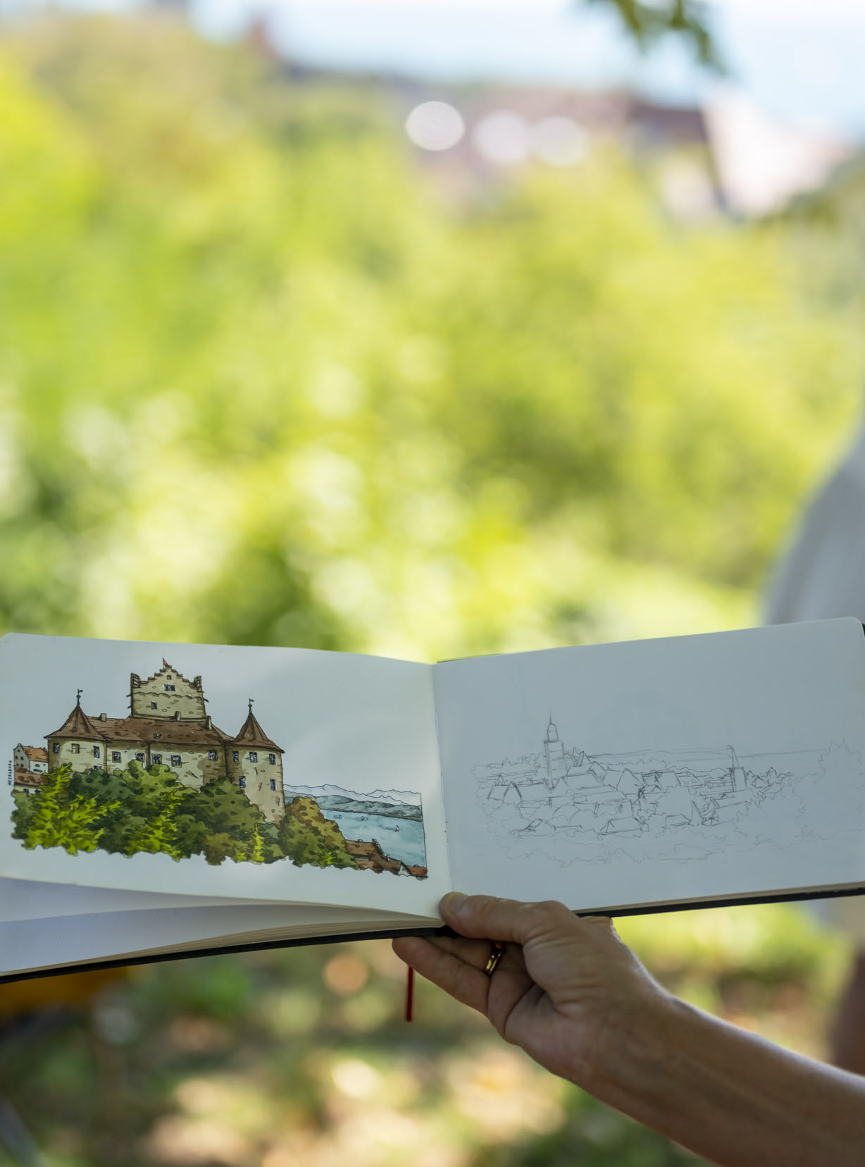 Ein offenes Skizzenbuch wird draußen vor das gesketchte Motiv gehalten