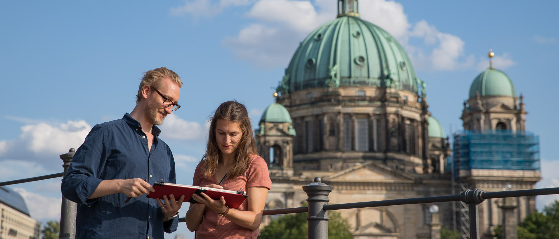 Ein Dozent steht mit einer Kursteilnehmerin vor dem Berliner Dom und erklärt ihr etwas in ihrem Skizzenbuch