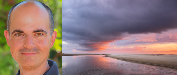 Ein lächelnder Mann (Foto-Dozent Helmut Kruse) neben einem seiner Werke (ein Foto von einer Küstenlandschaft am Strand bei Sonnenuntergang)
