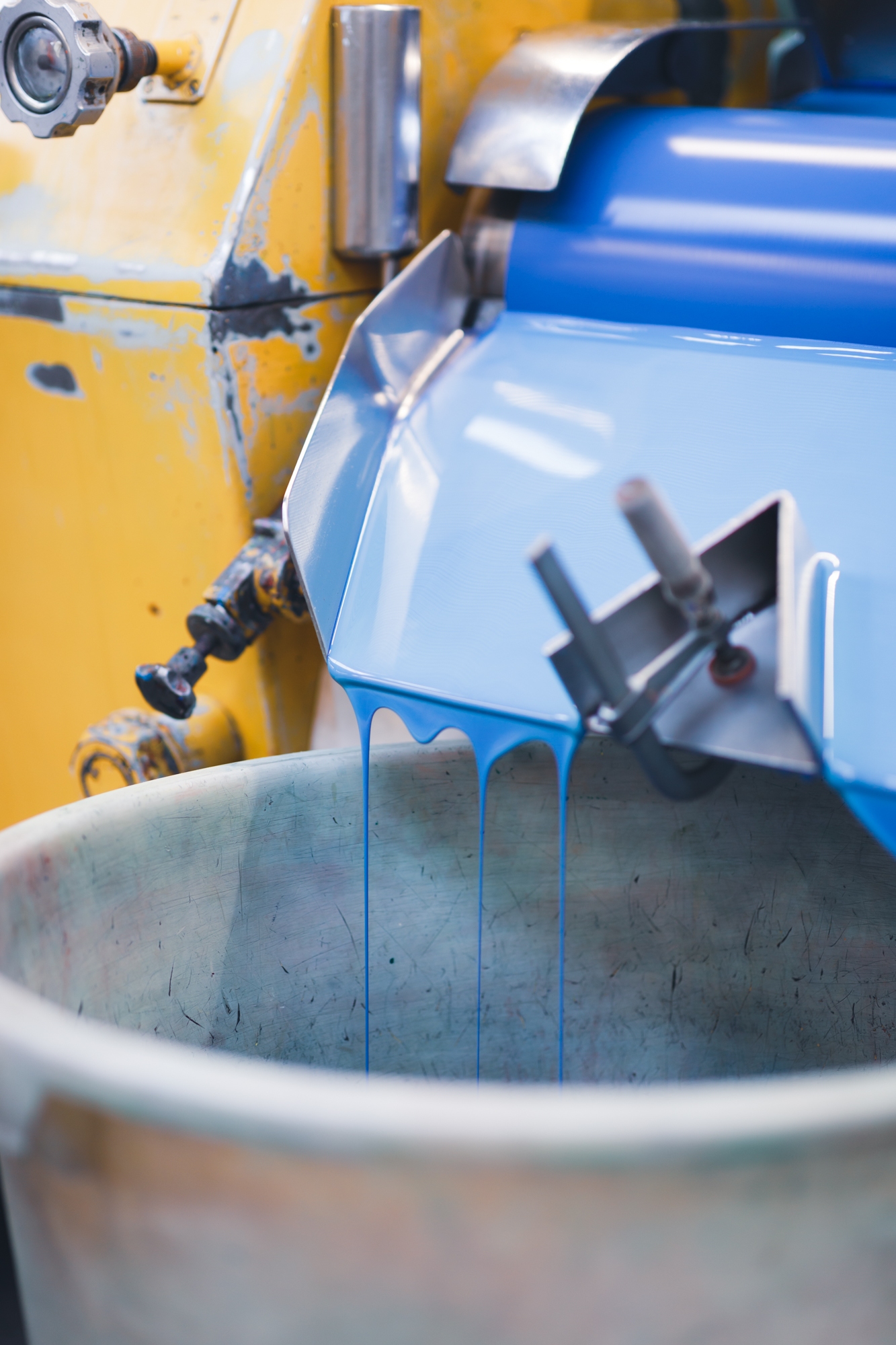Blaue Farbe fließt von einer Farbwalze in einen Bottich.